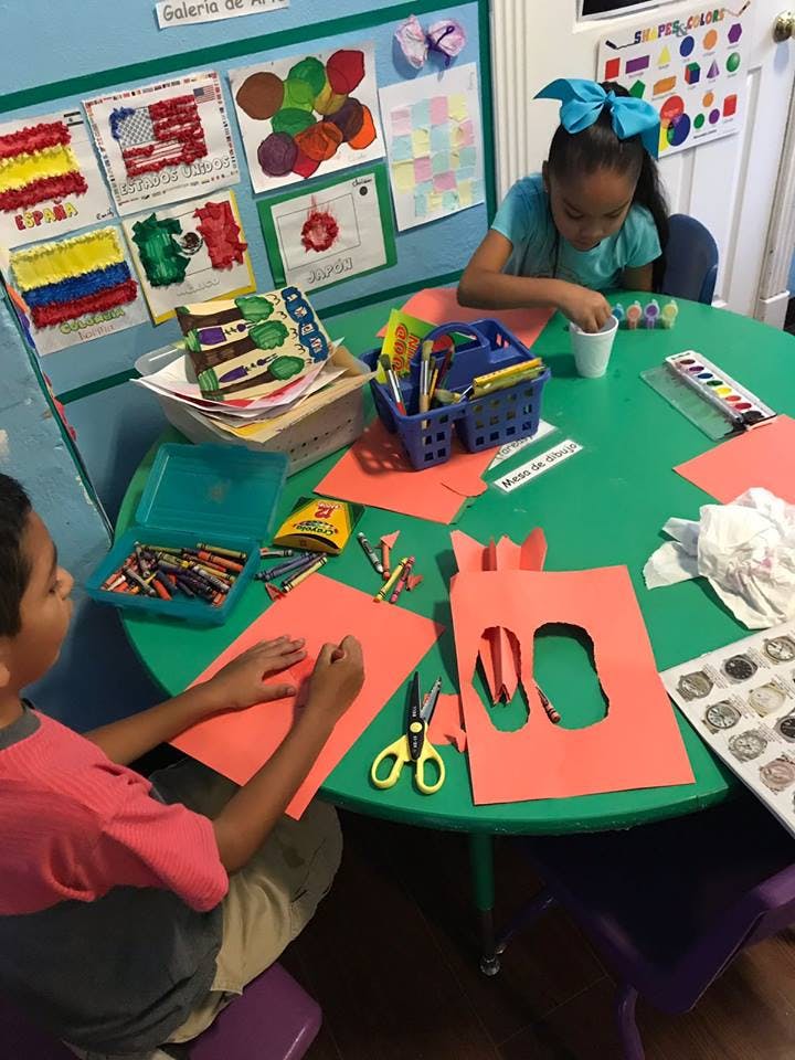 Two children doing crafts at a green table in a classroom