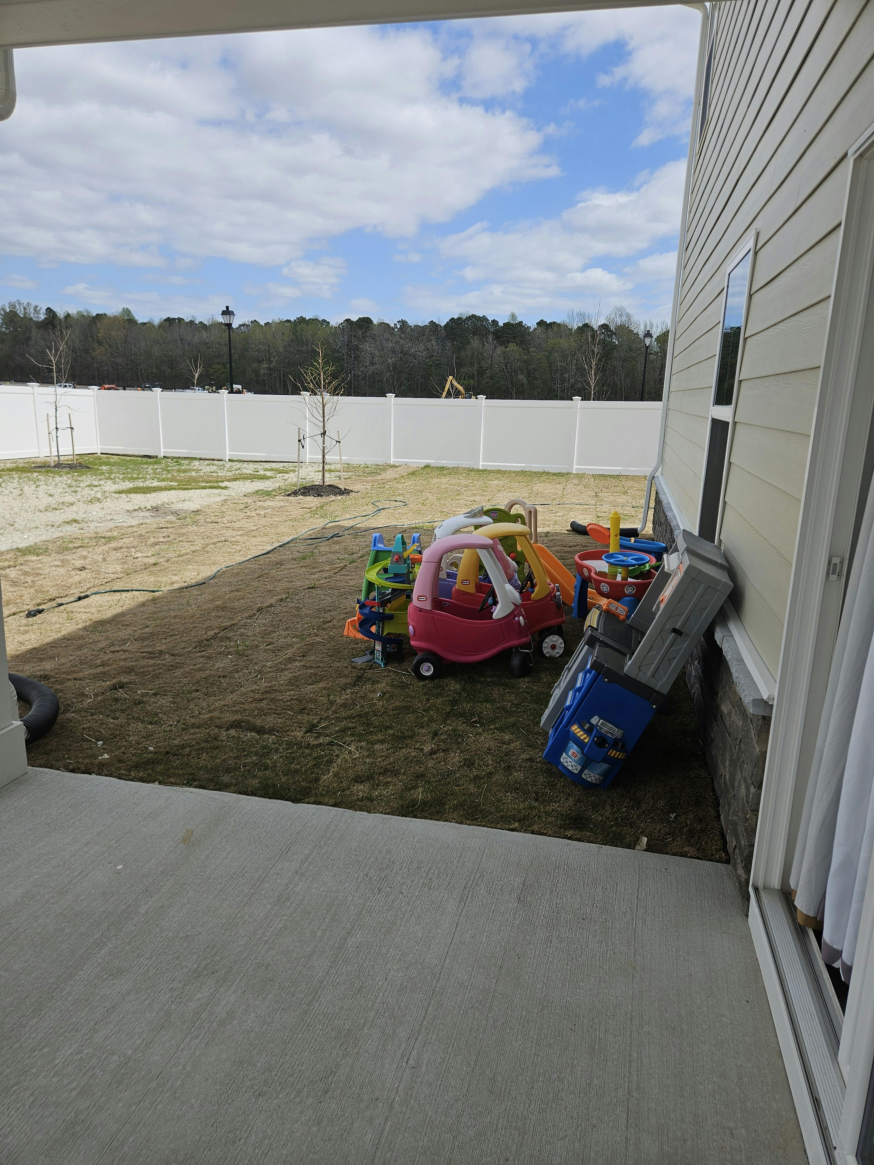 Children's toys, including a play truck and car, on grass next to a house
