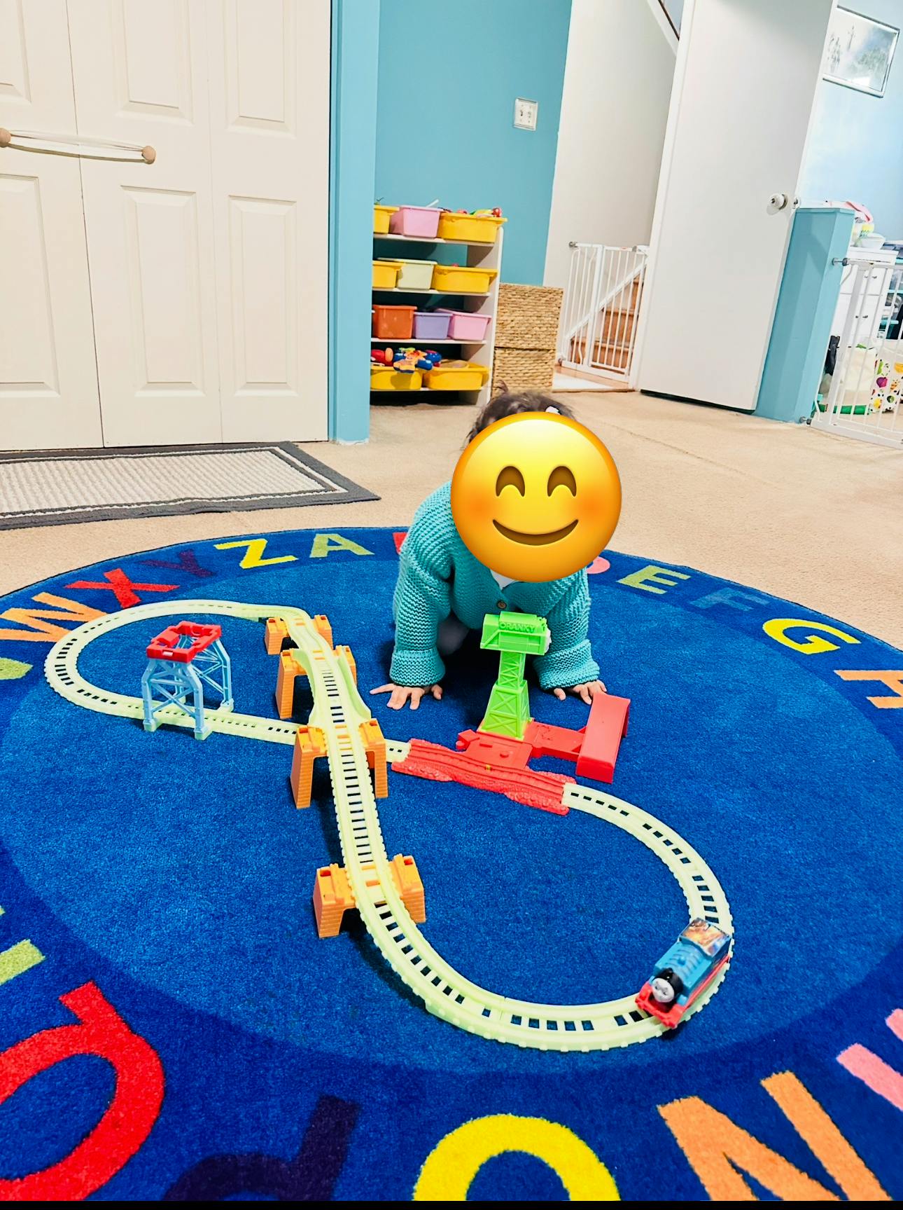 Child playing with a toy train set on a blue alphabet rug
