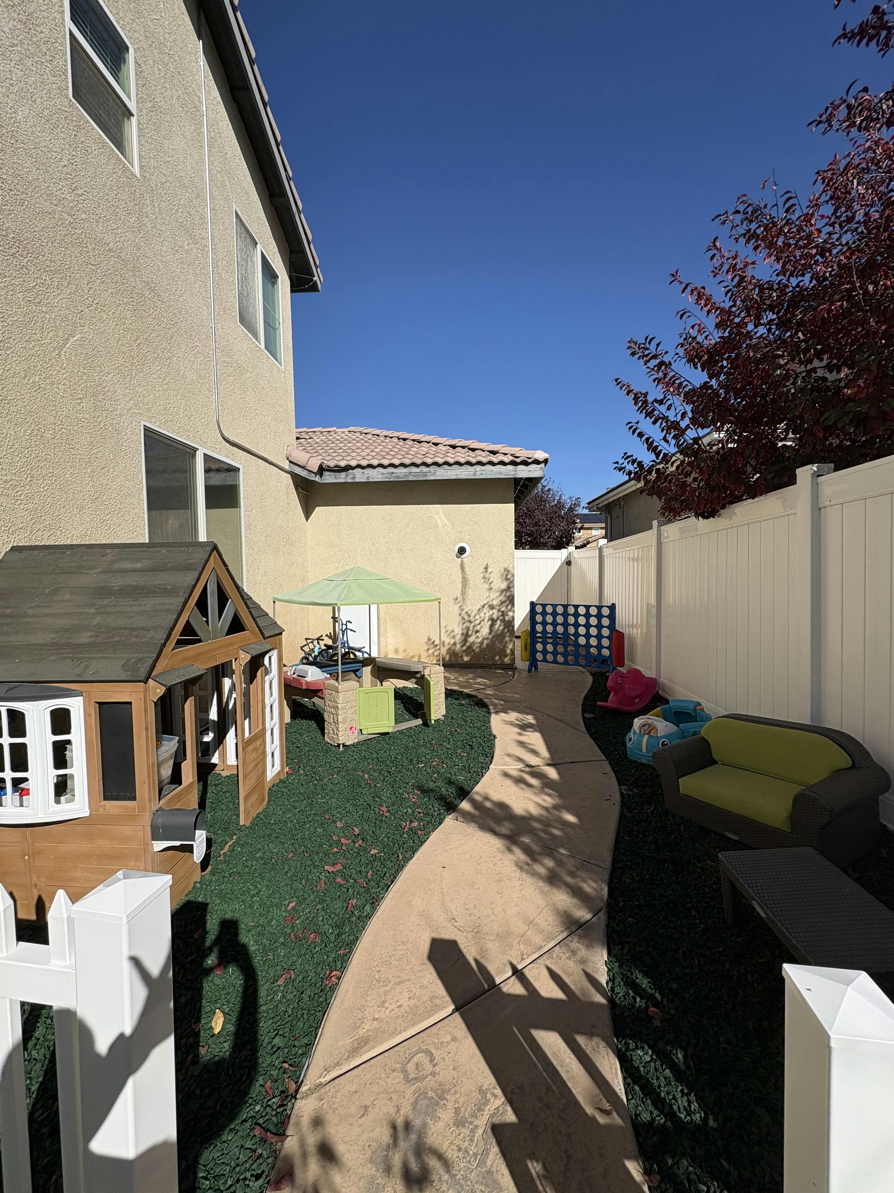 backyard play area with a playhouse, green umbrella, and a concrete path