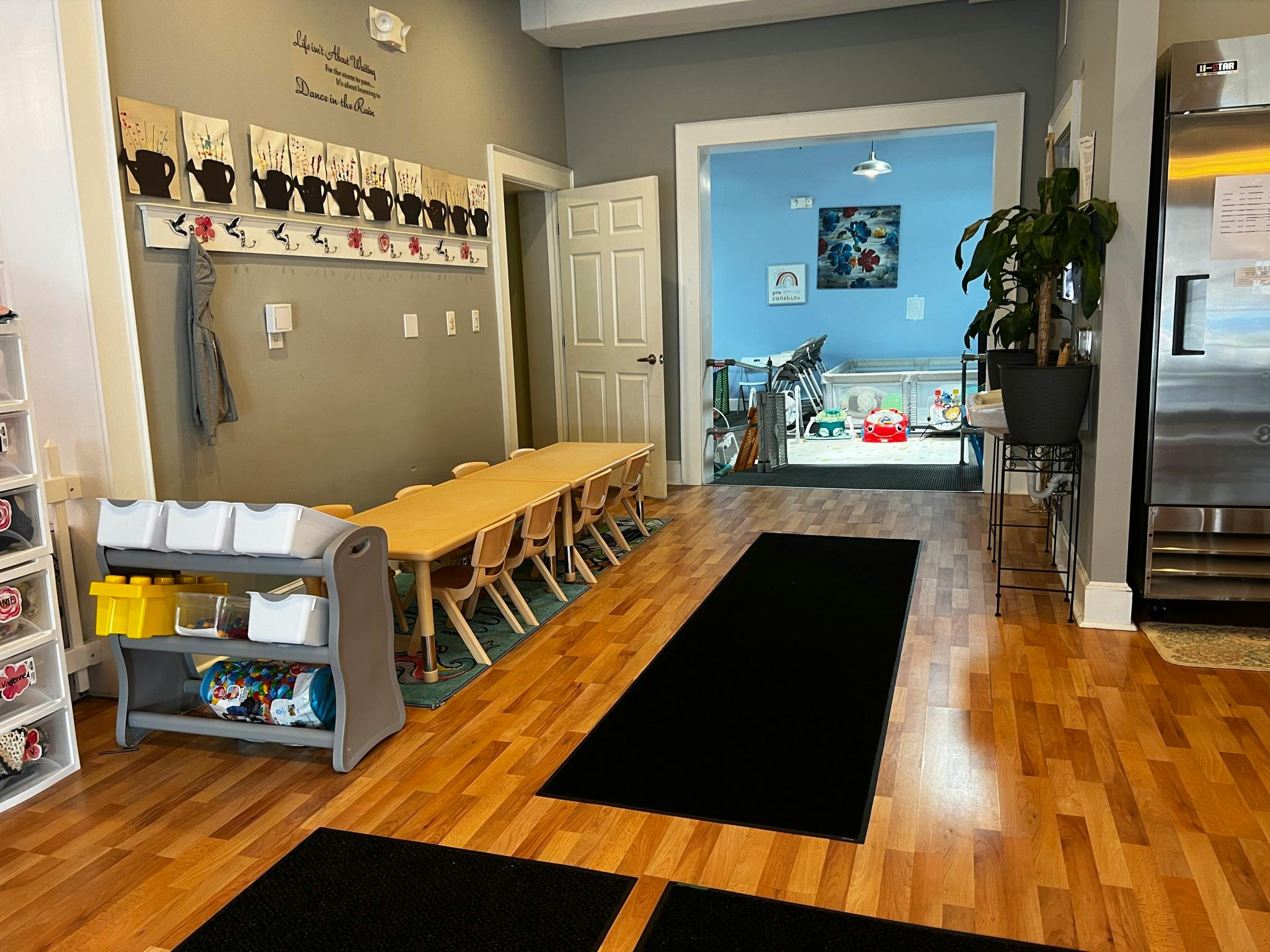 Classroom with long table and chairs, toy storage, and open doorway to another room