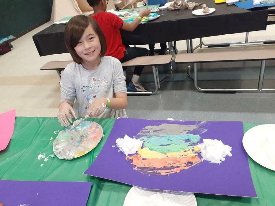 Child with paint on hands and a purple paper with colorful paint