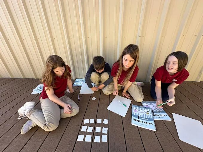 Four children sitting on a deck with papers and cards