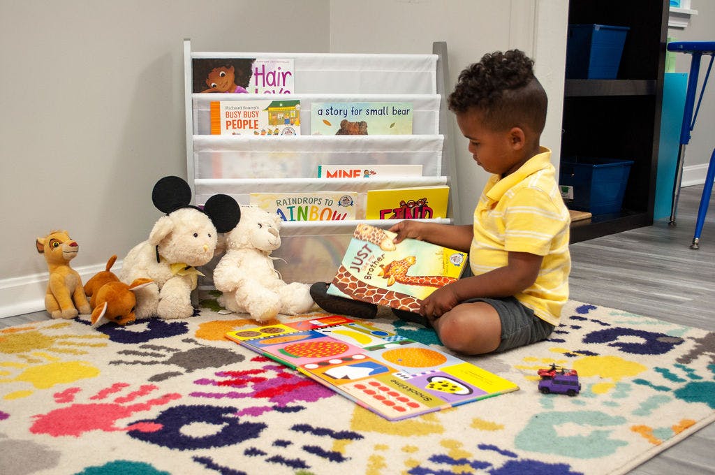 Child sitting on a rug reading a book next to stuffed animals