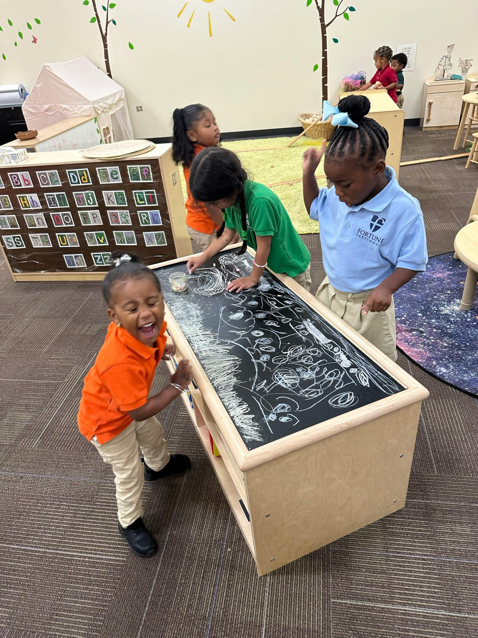 Children drawing on a large chalkboard table in a classroom