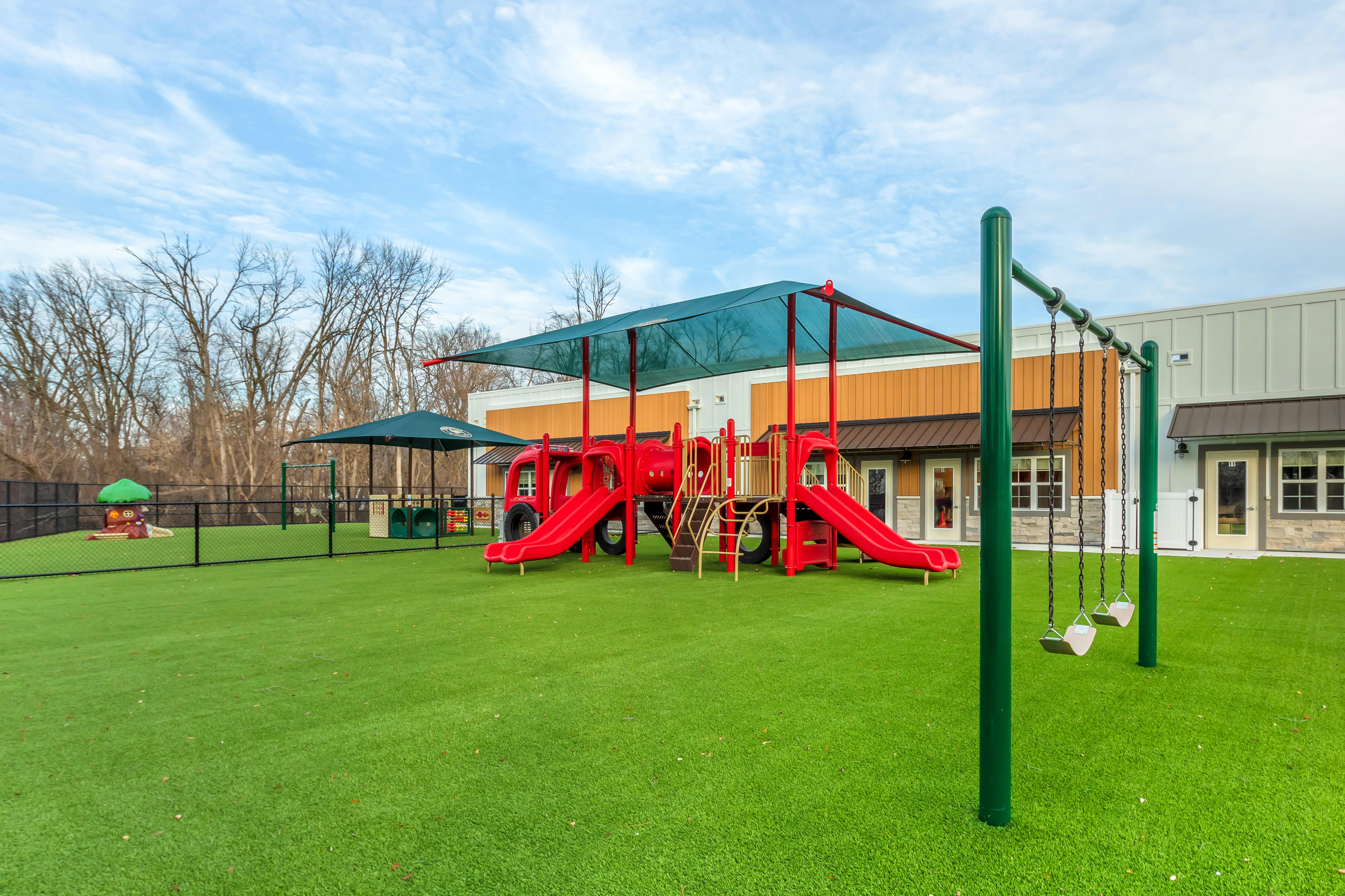 A red playground structure with slides and a green swing set on artificial grass