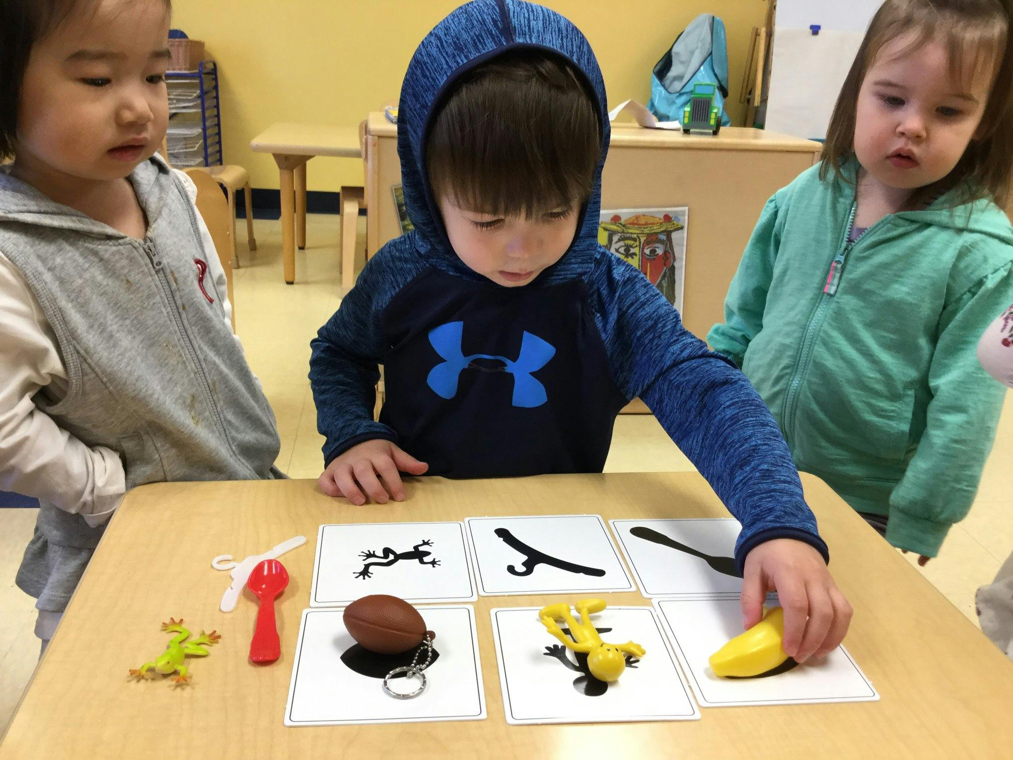 Three children playing with matching cards and small objects onjects on a table