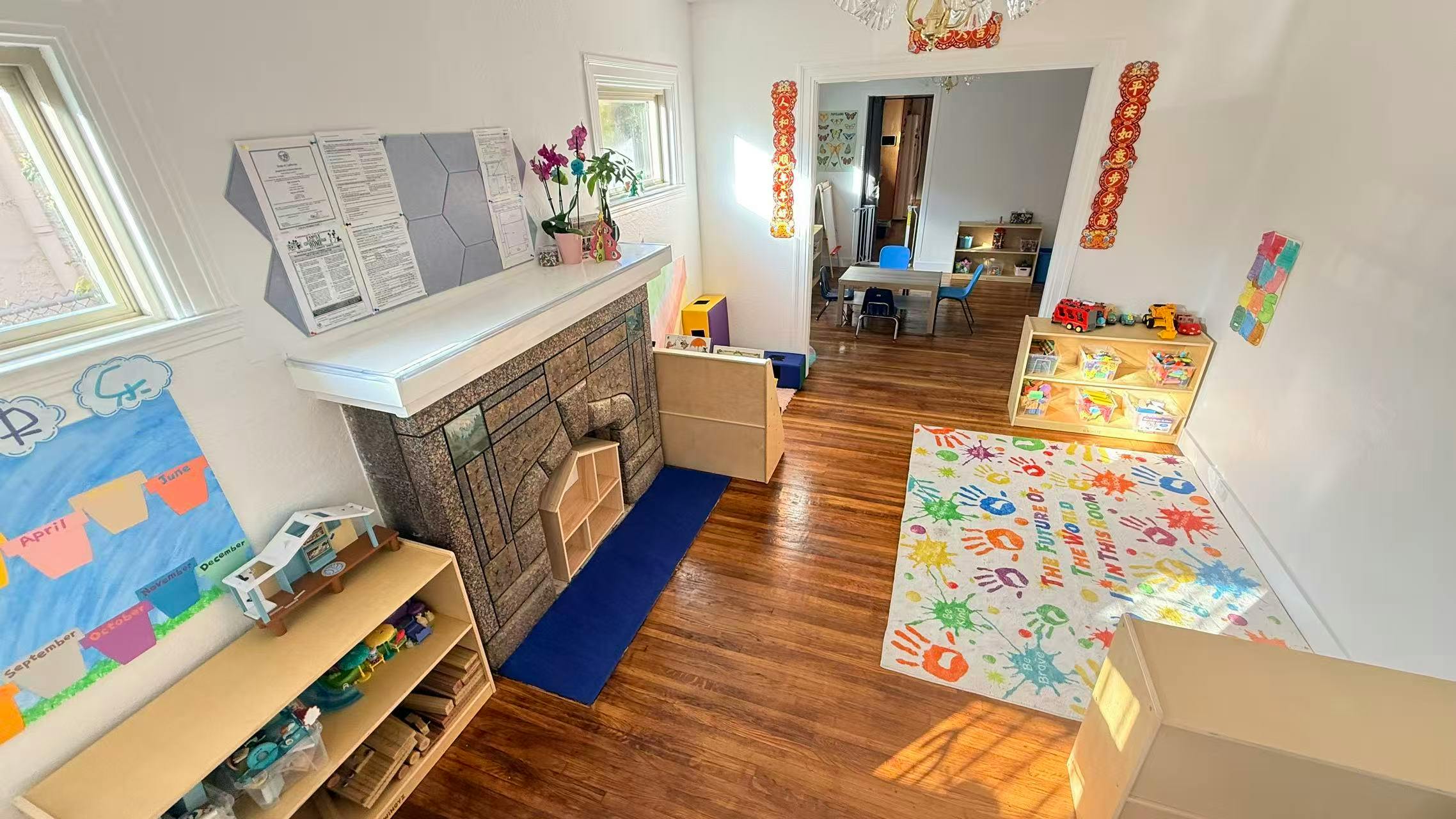Childcare classroom with toys, a fireplace, and a colorful rug with handprints