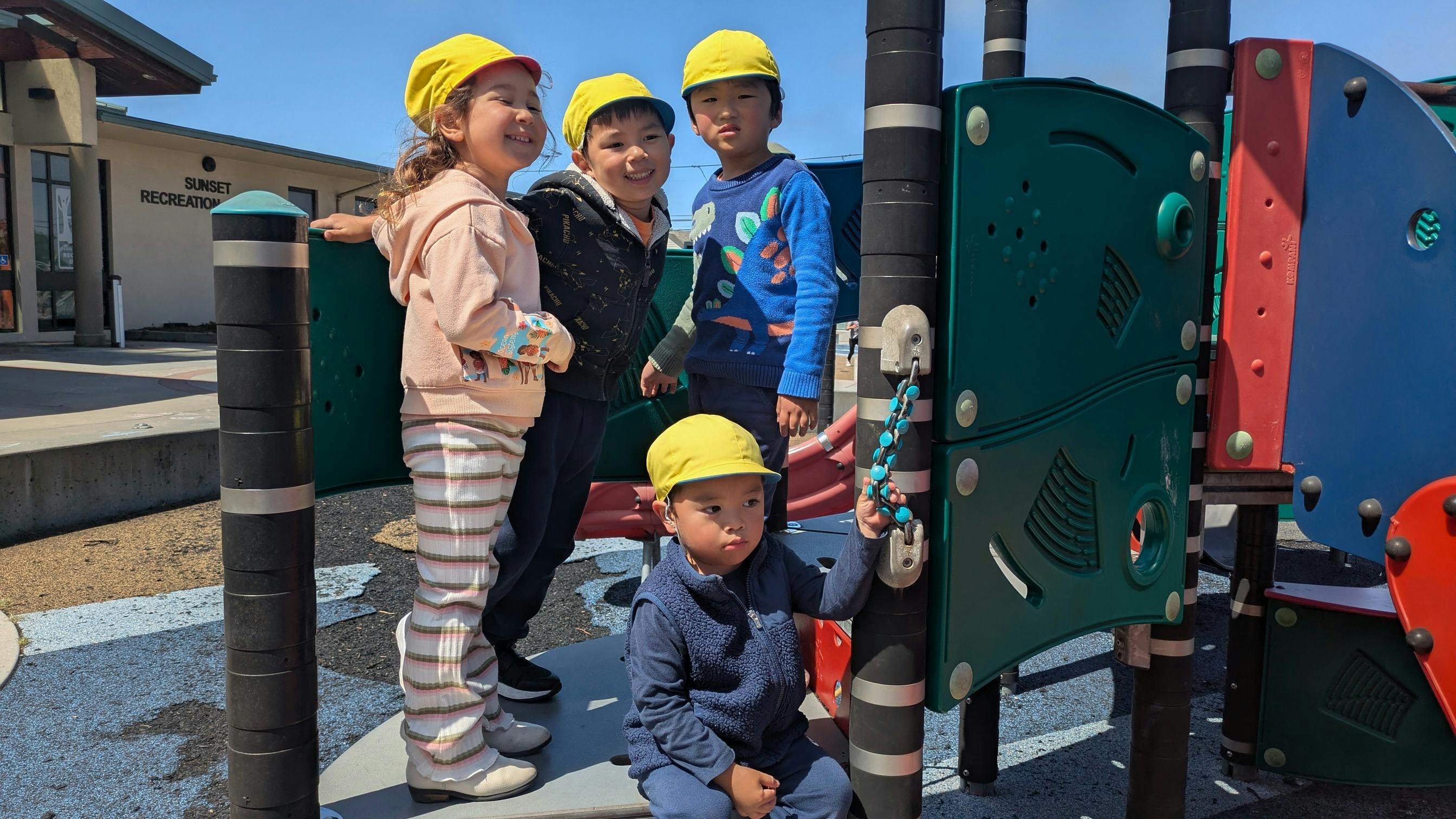 Four children in yellow hats playing on an outdoor playground structure