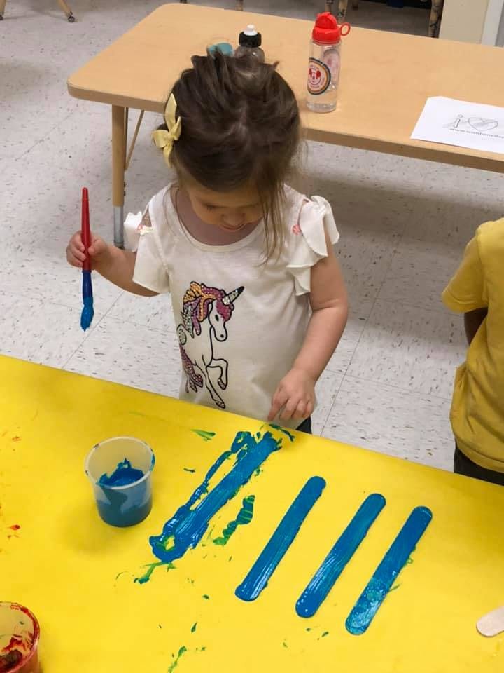 Child painting blue lines on a yellow surface with a paintbrush