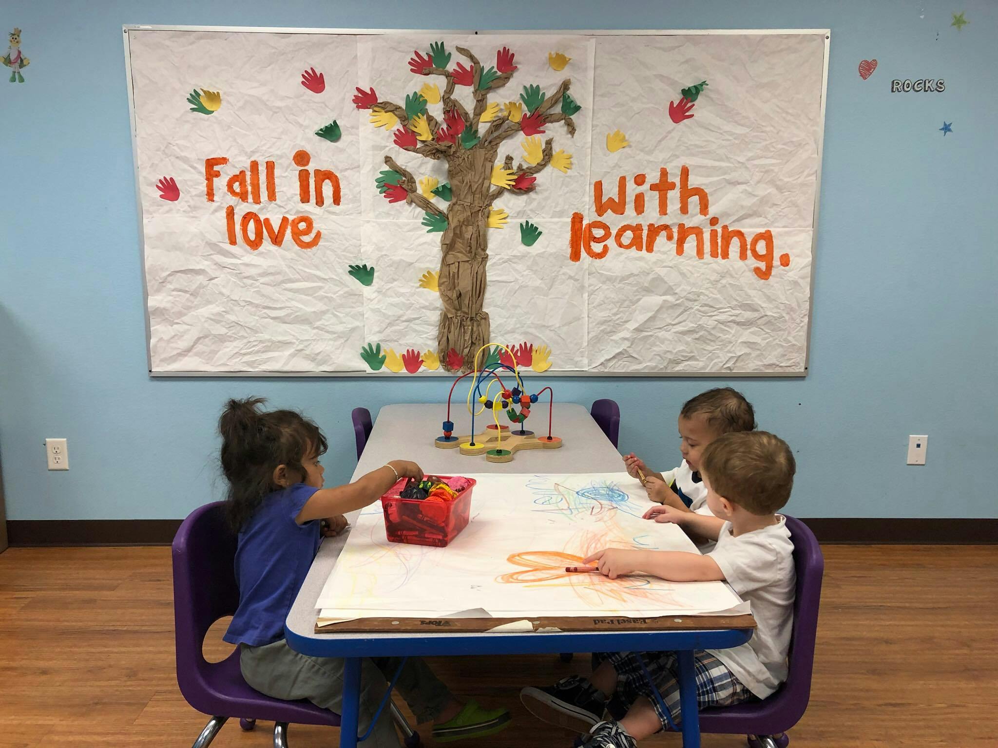 Three children at a table with art supplies and a sign that says "Fall in love with learning"