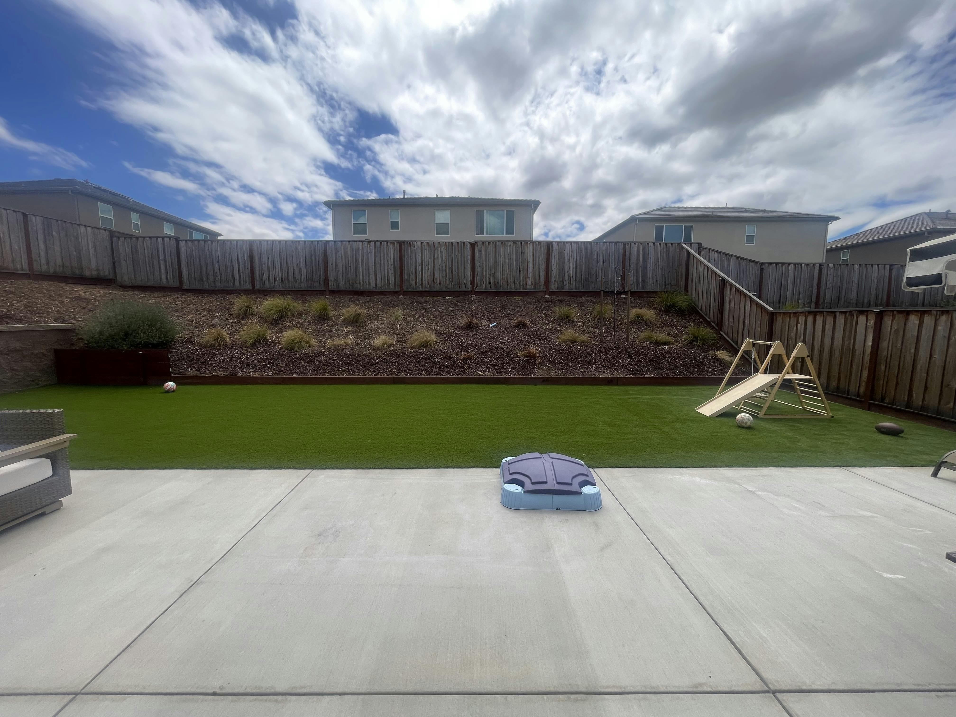 Backyard with artificial turf, a children's play set, and a plastic sandbox