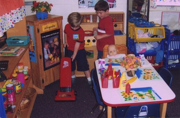 Two children playing with a toy vacuum in a classroom