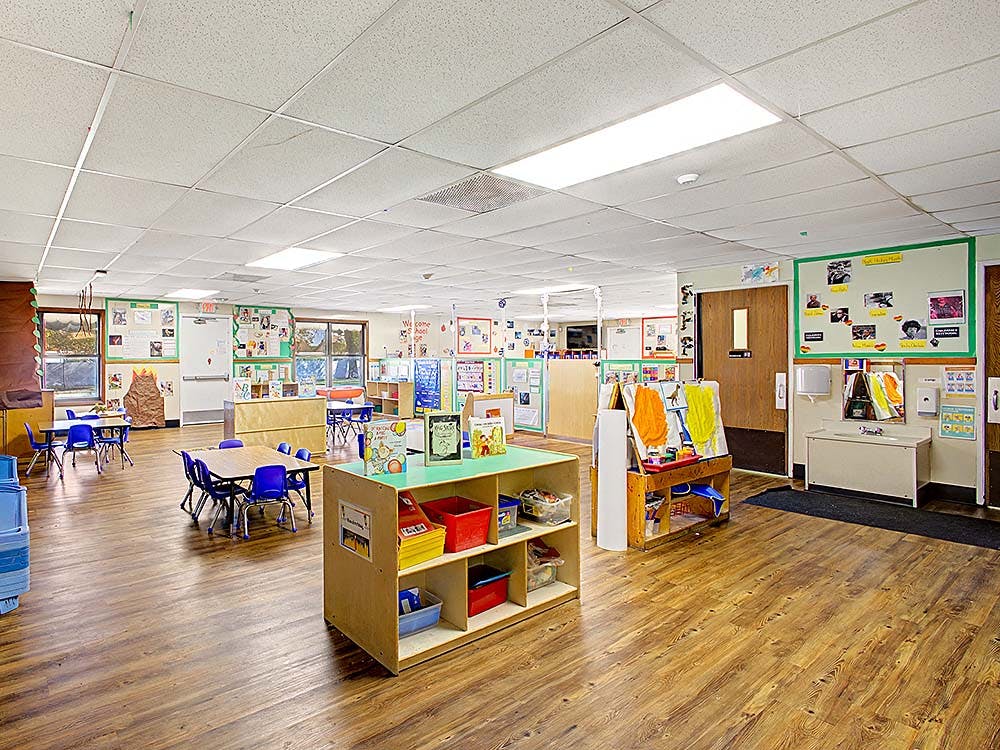 Empty classroom with small tables and chairs, shelves, and art easels