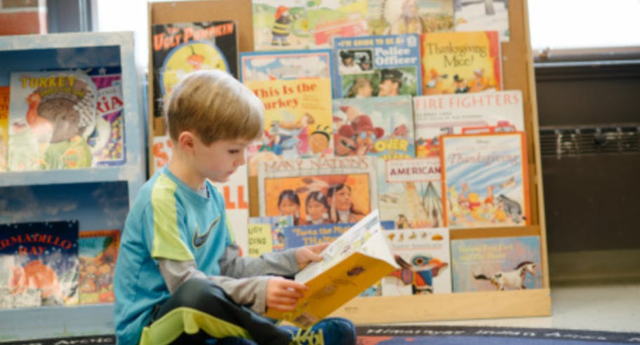 Child sitting on floor reading a book in front of a book display