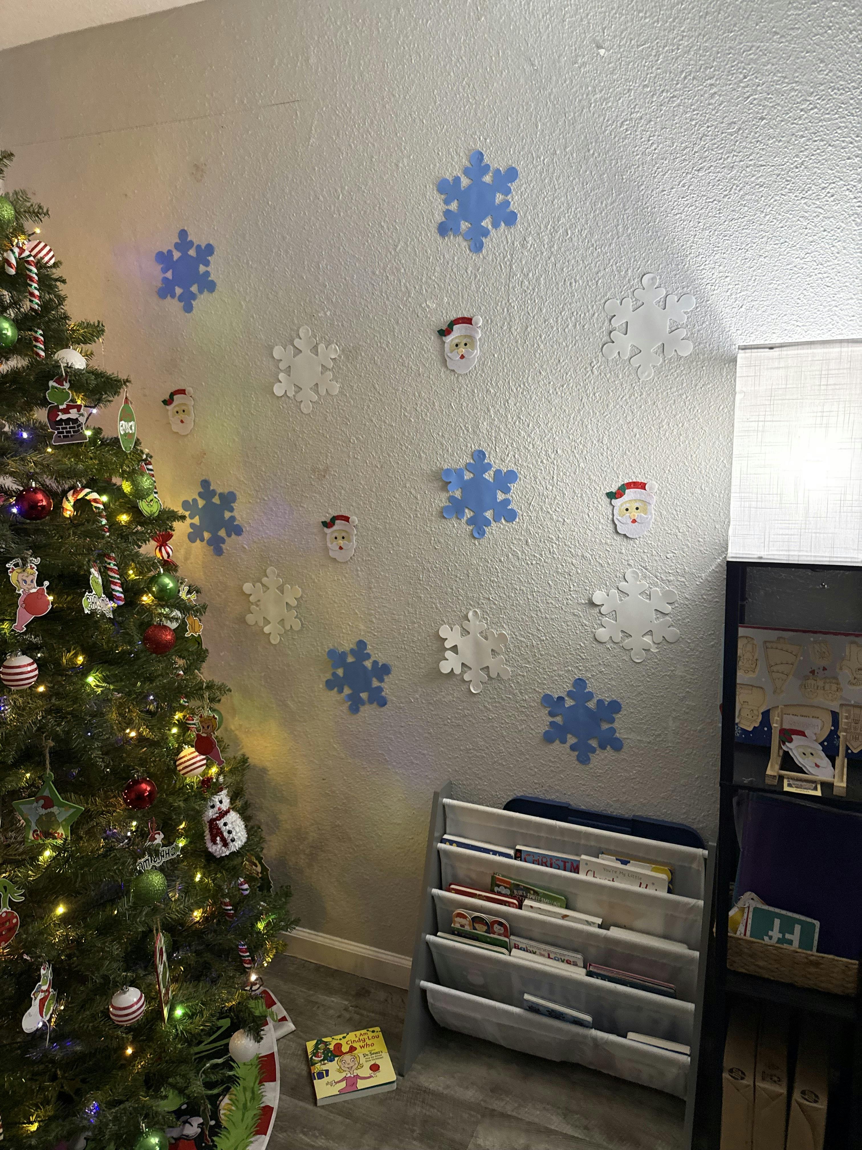 Decorated Christmas tree next to a wall with paper snowflakes and Santa cutouts