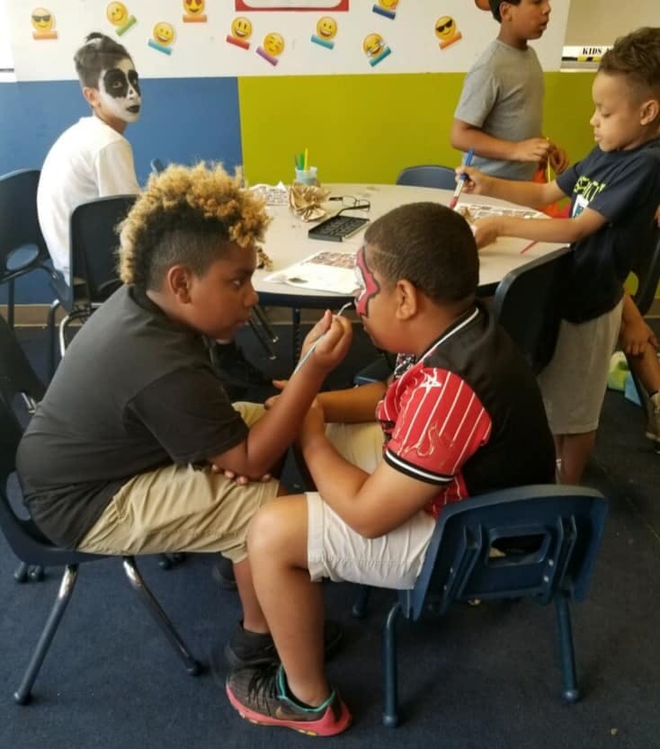 Child painting another child's face in a classroom