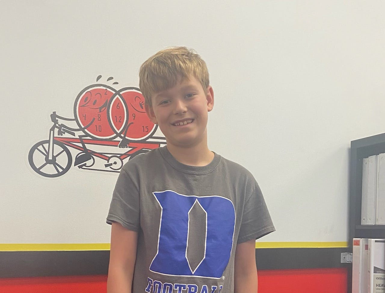 Child smiling and wearing a gray shirt with a blue letter D