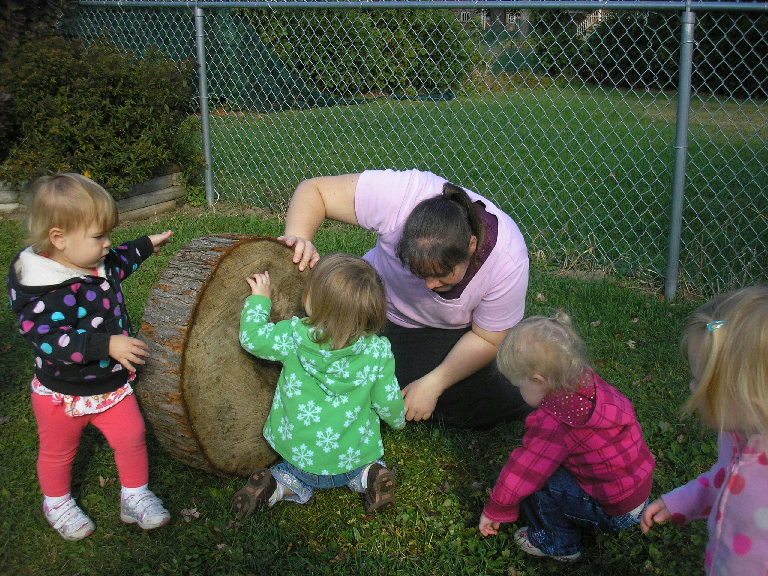 Person and multiple children interacting with a large log section of a tree trunk