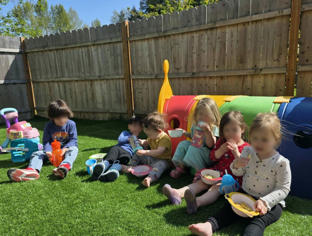 Children sitting on grass eating snacks in a backyard eating from a low angle
