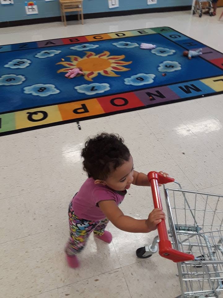 Child pushing a toy shopping cart in a room with an alphabet rug