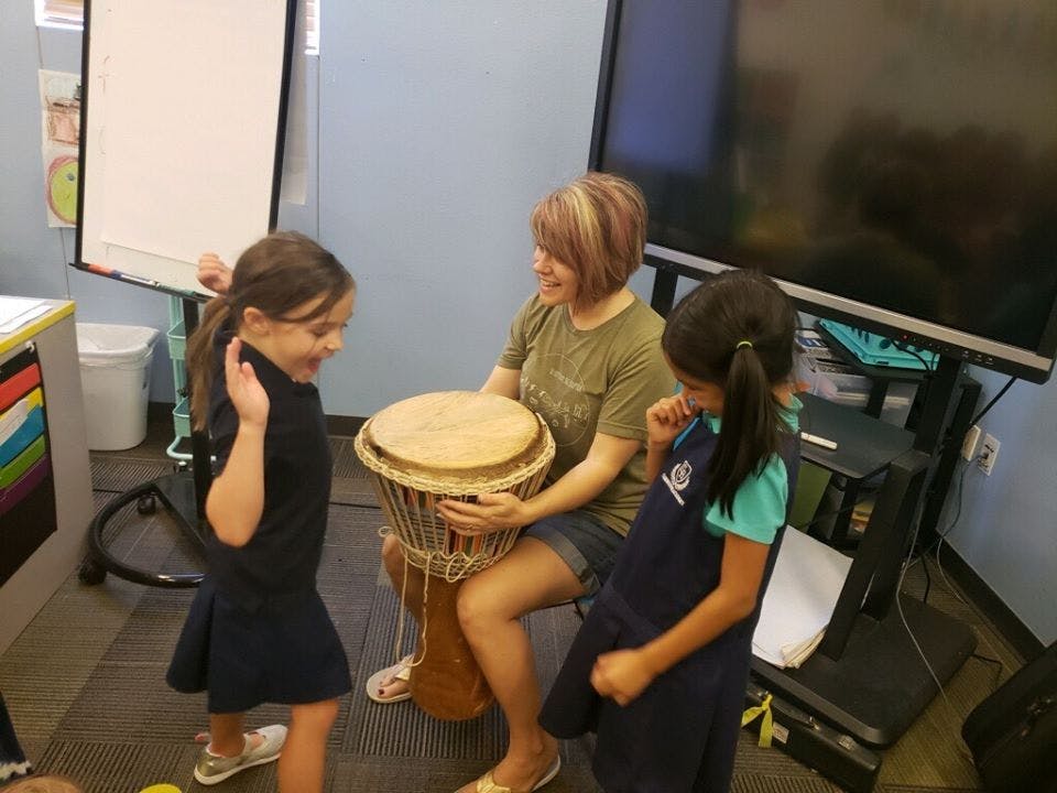 Person playing a drum with two children watching