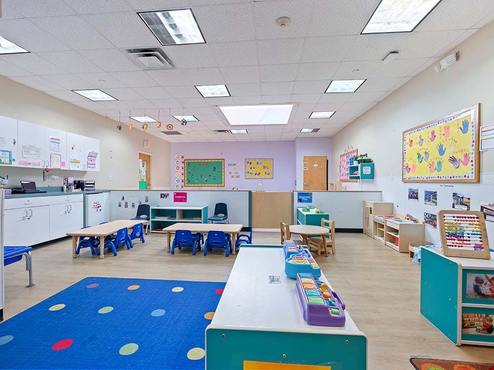 Empty classroom with small tables and chairs, and play equipment