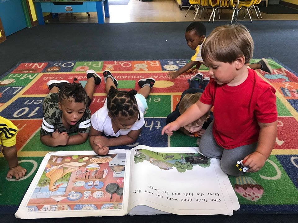Children on a rug looking at an open book
