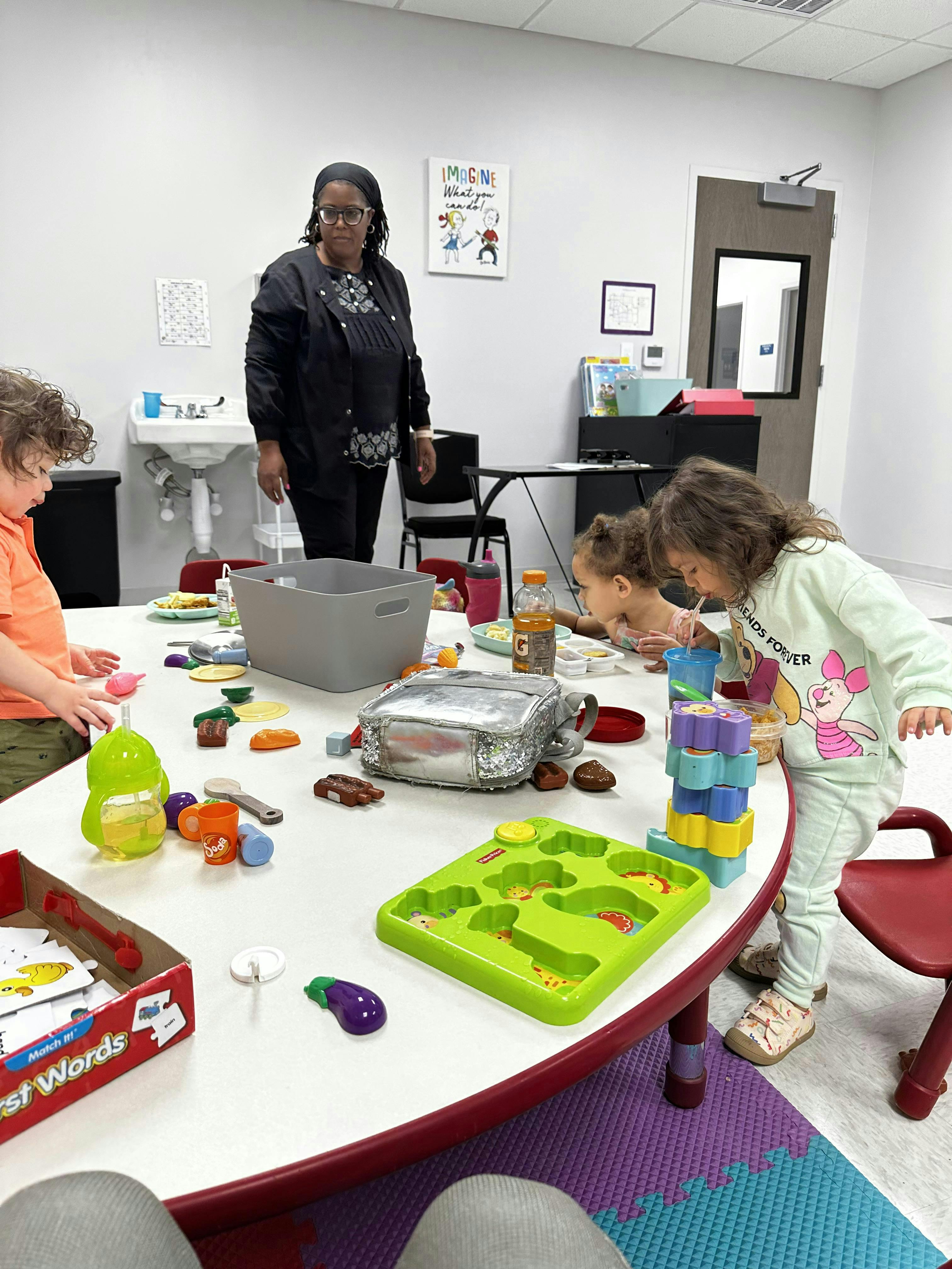 Adult standing behind a table where children are playing with toys