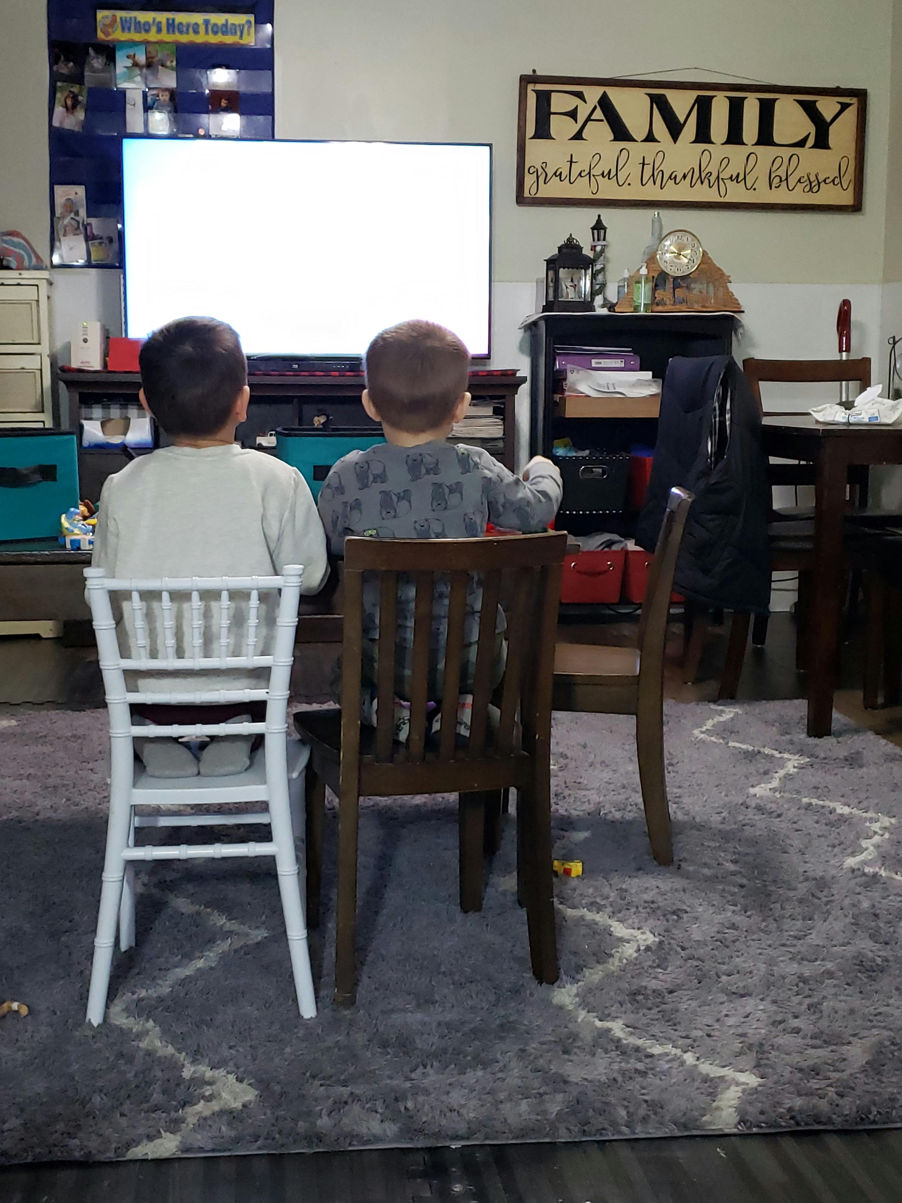 Two children sitting in chairs watching a television
