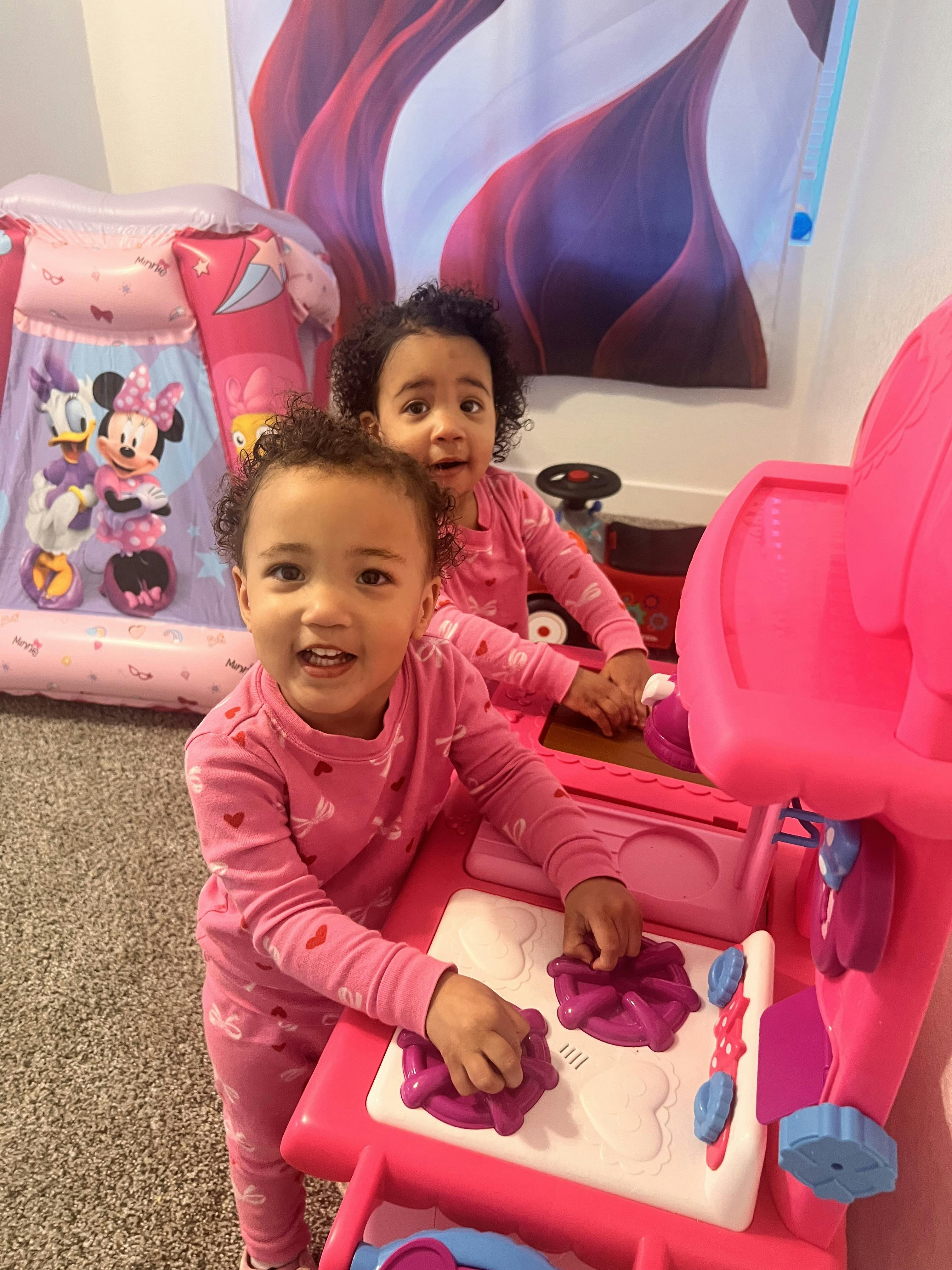 Two children playing with a pink toy kitchen set