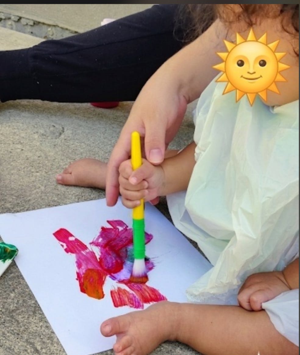 Adult hand helping a child paint on paper