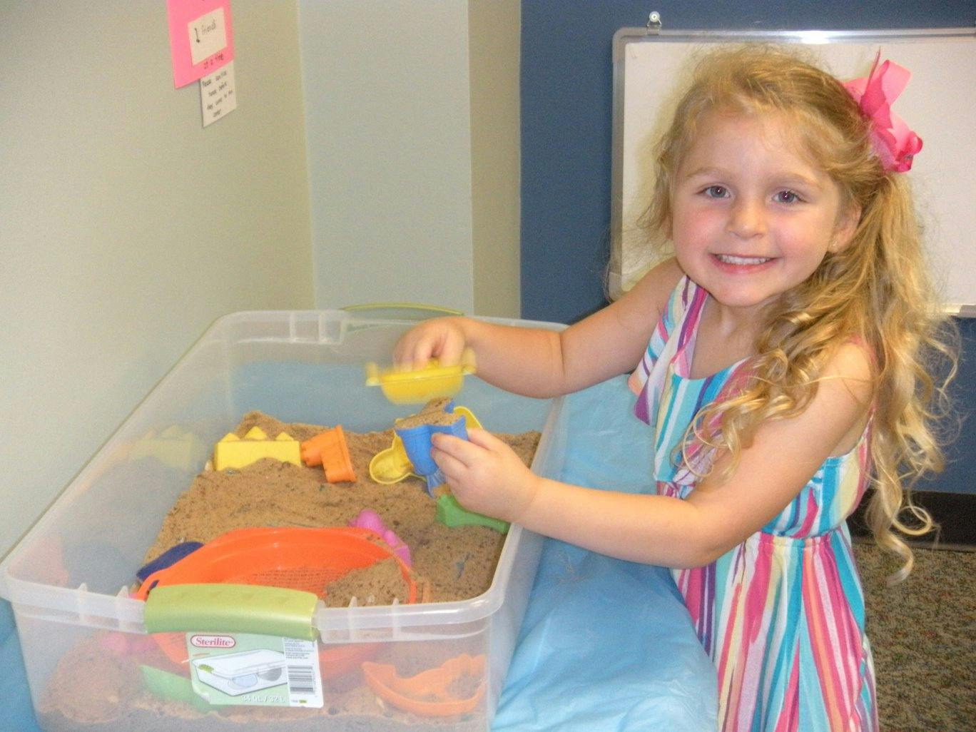 Child playing with sand and toys in a clear bin