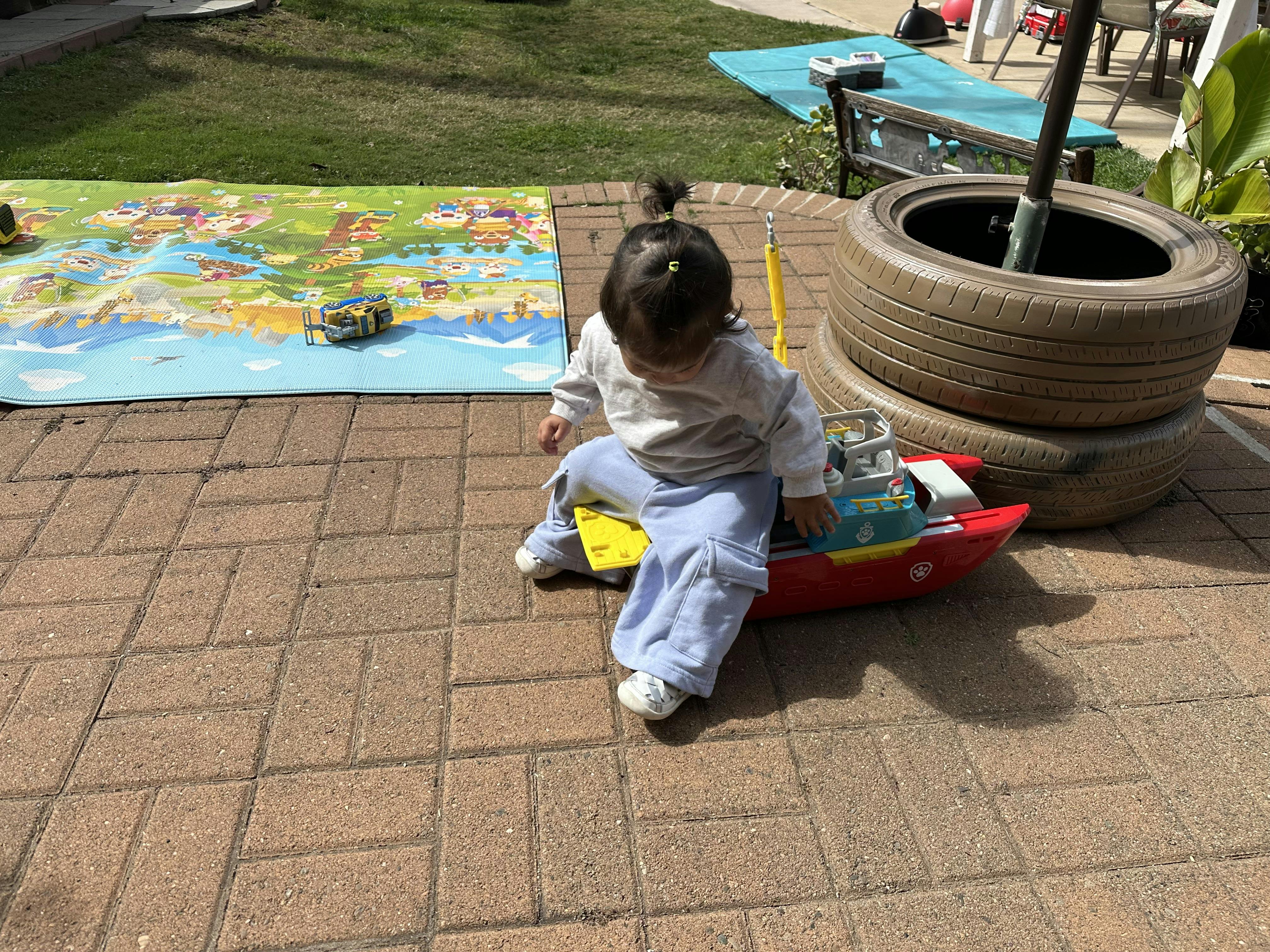 Child sitting on a red toy boat on a paved patio