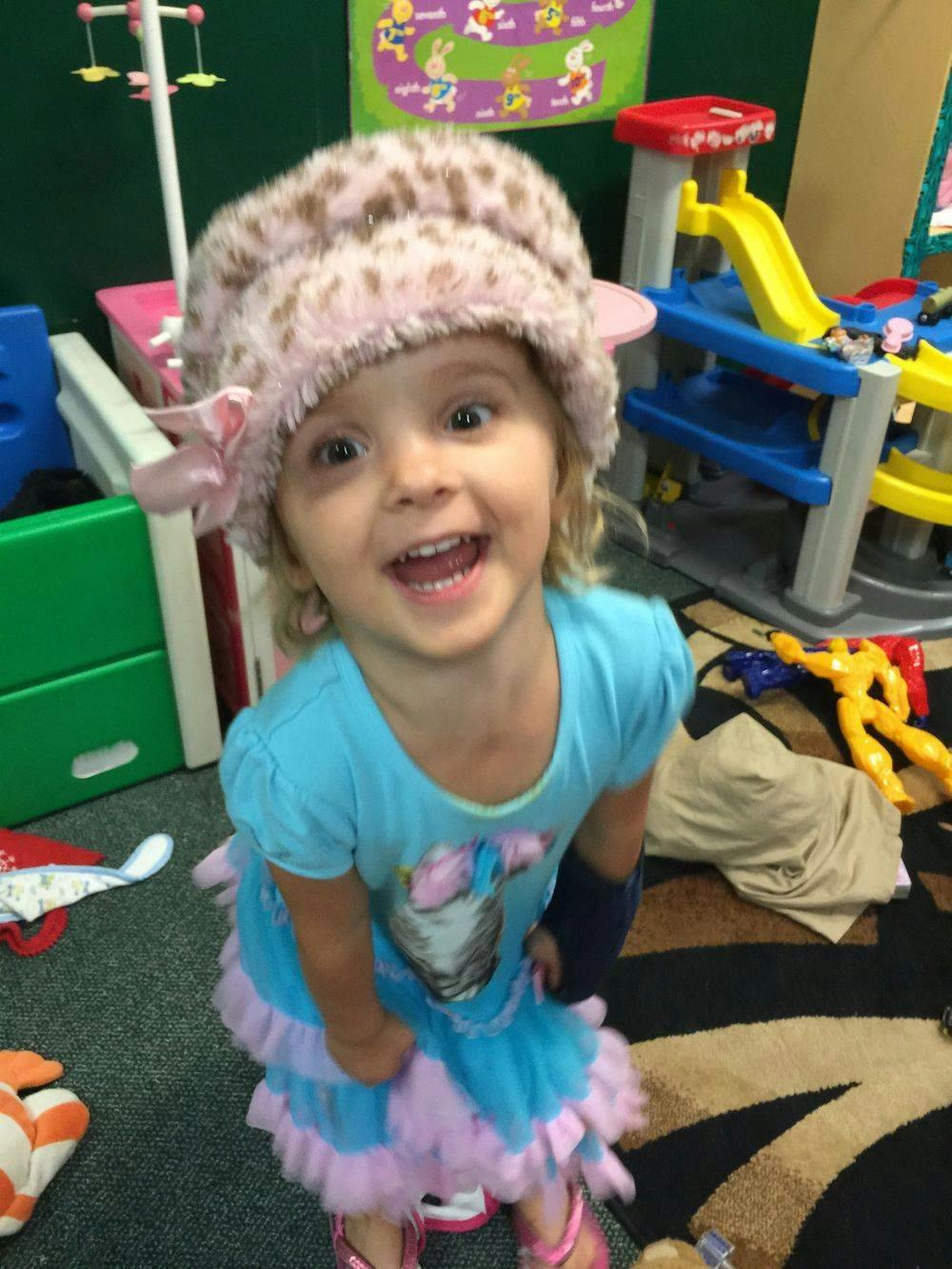 Child wearing a fuzzy hat and a blue dress with a cast on their arm