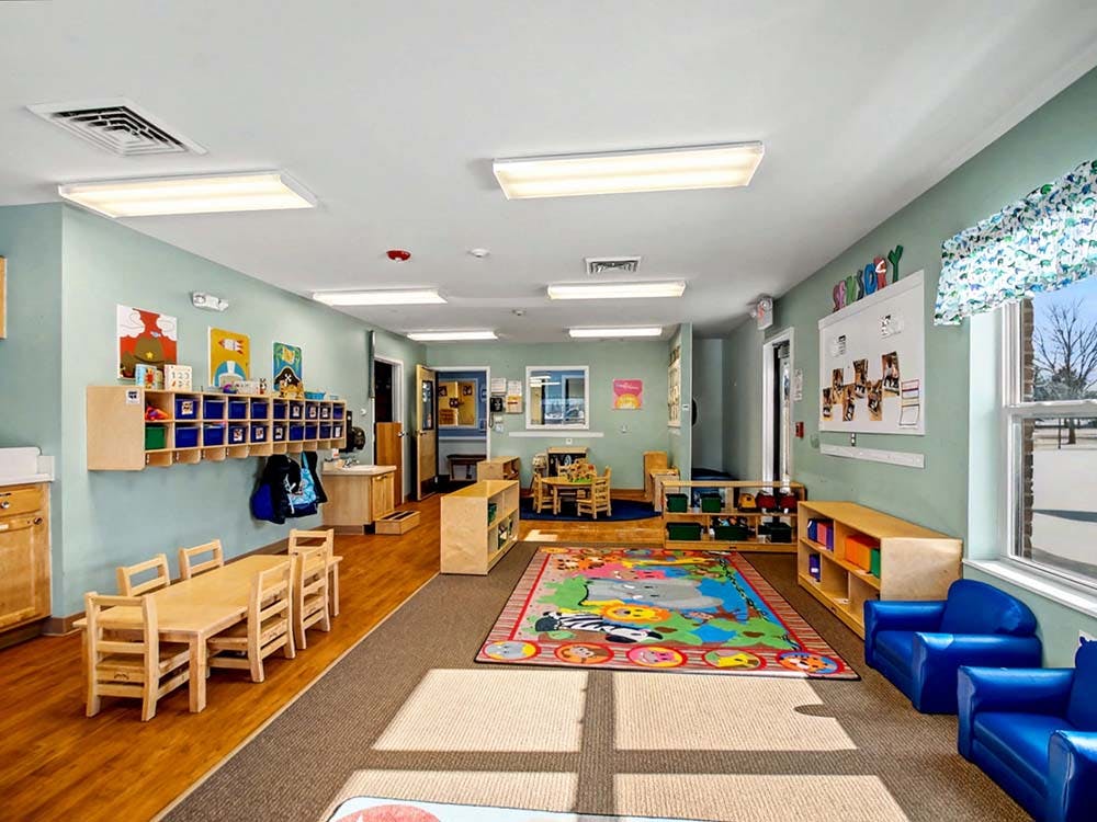 An empty early childhood classroom with small tables, chairs, and play areas