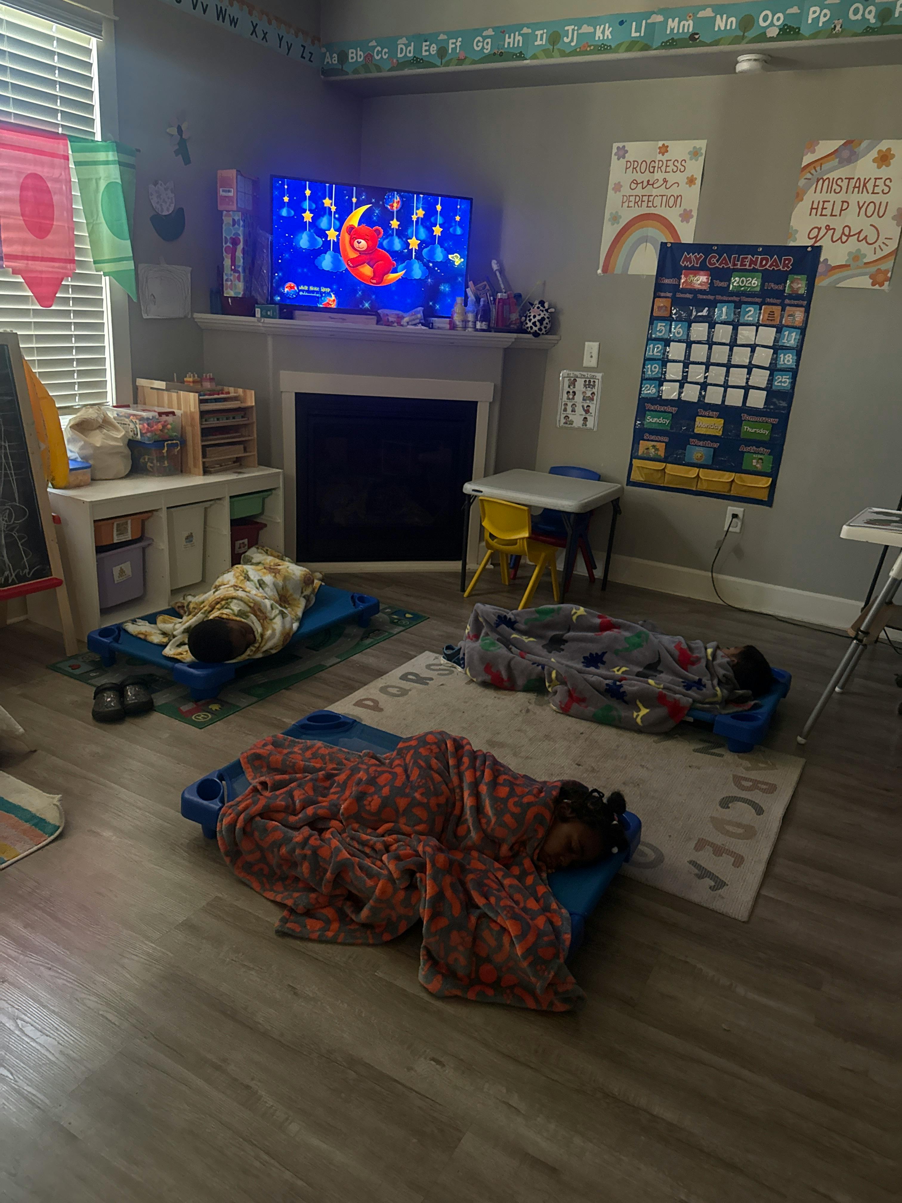 Three children sleeping on cots on the floor in a classroom