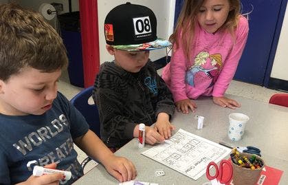 Three children at a table doing an activity with paper and glue sticks