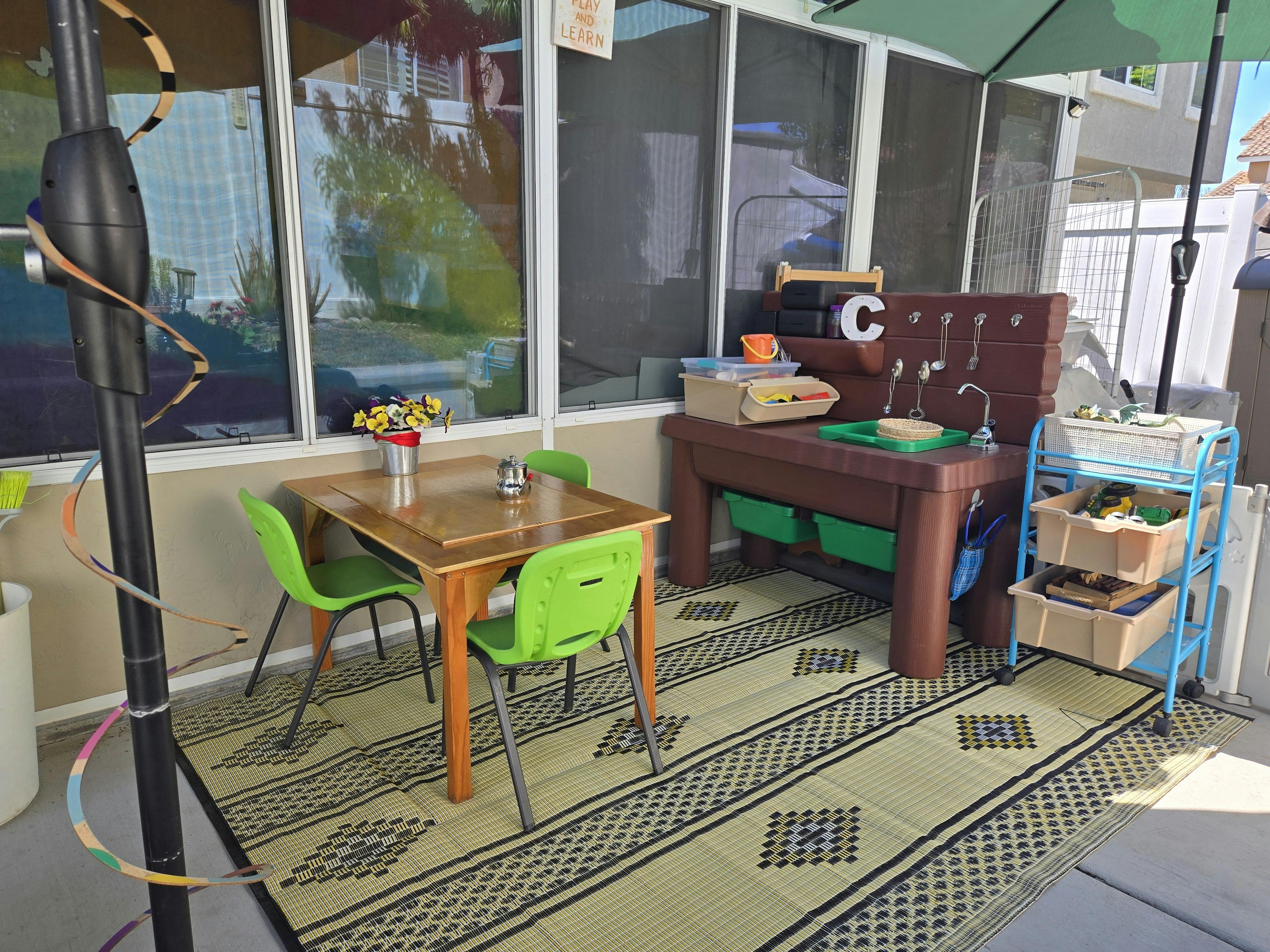 A playroom setup on a patio with a children's table and chairs, and a play kitchen
