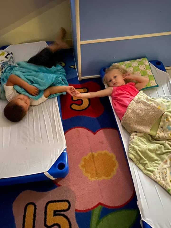 Two children lying on cots holding hands
