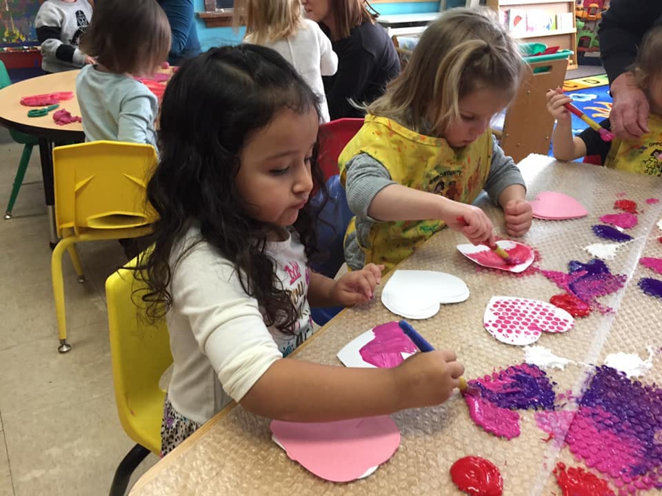Two children painting heart shapes at a table