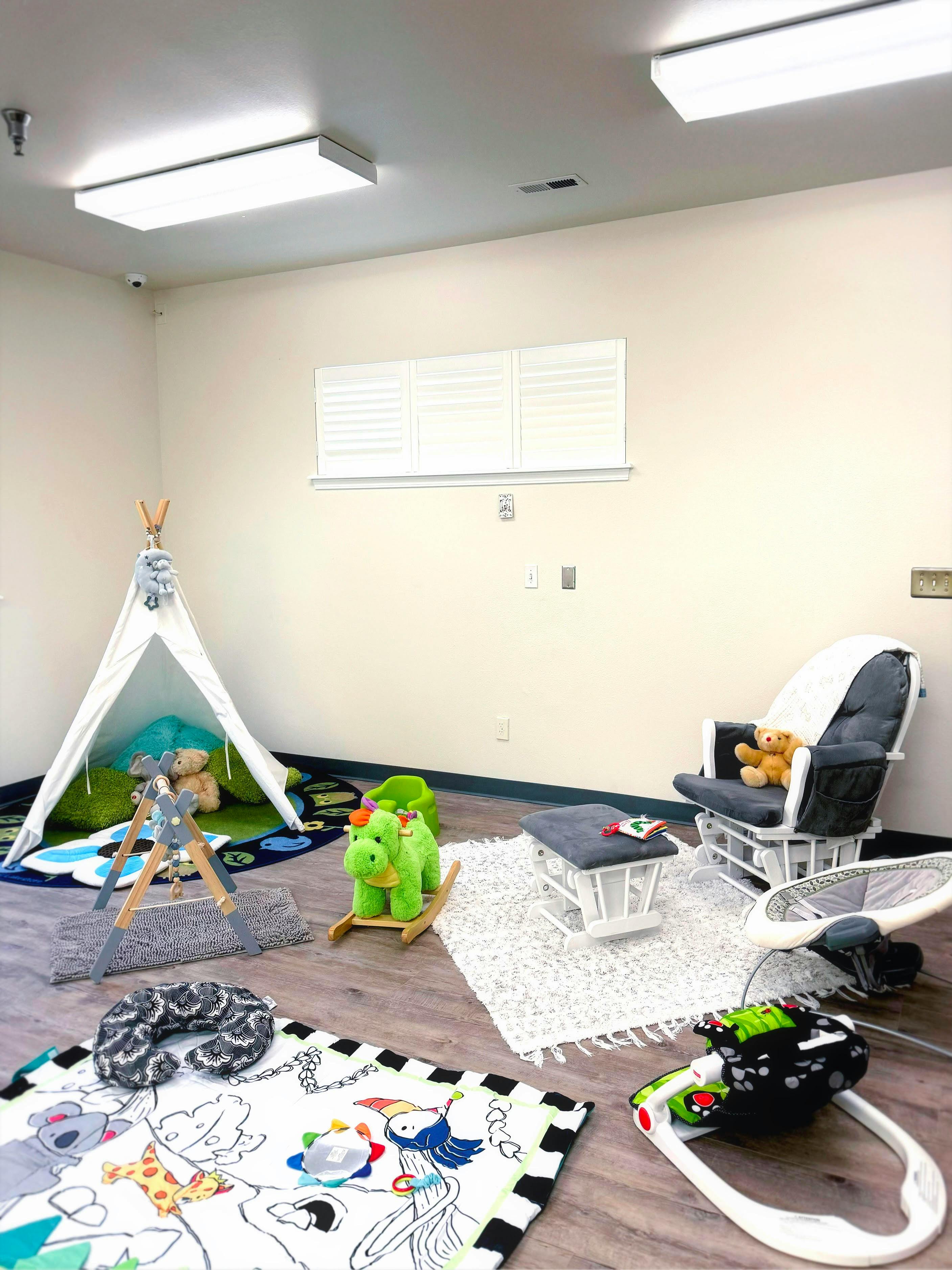 Playroom with a teepee, rocking horse, glider chair, and play mats