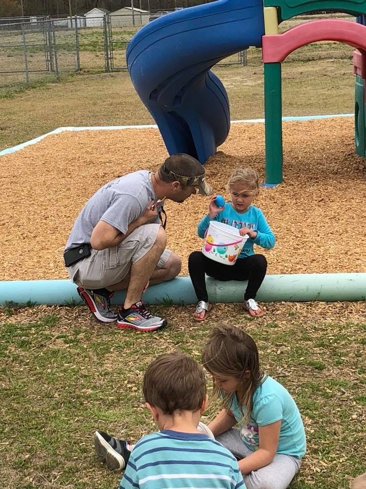 Person kneeling next to a child holding a bucket on a playground
