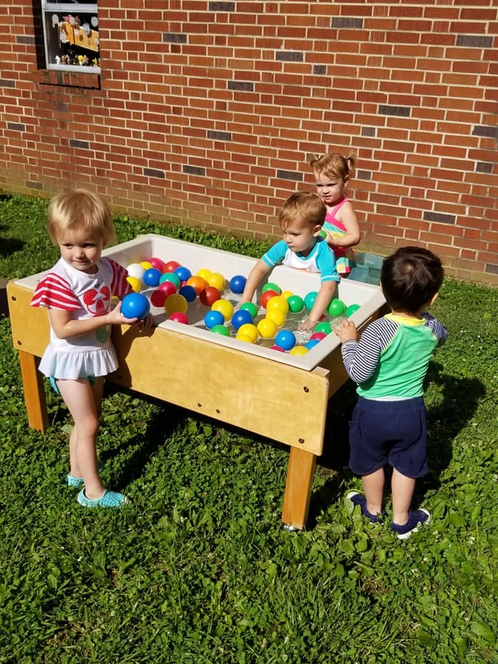 Children playing with colorful balls in a water table outdoors