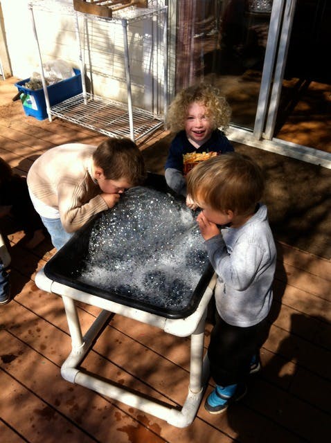 Three children playing with bubbles in a water table
