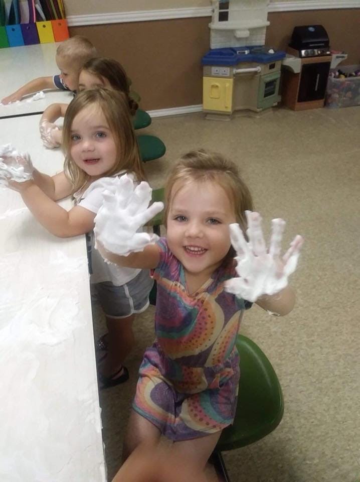 Two children with foamy hands in a classroom