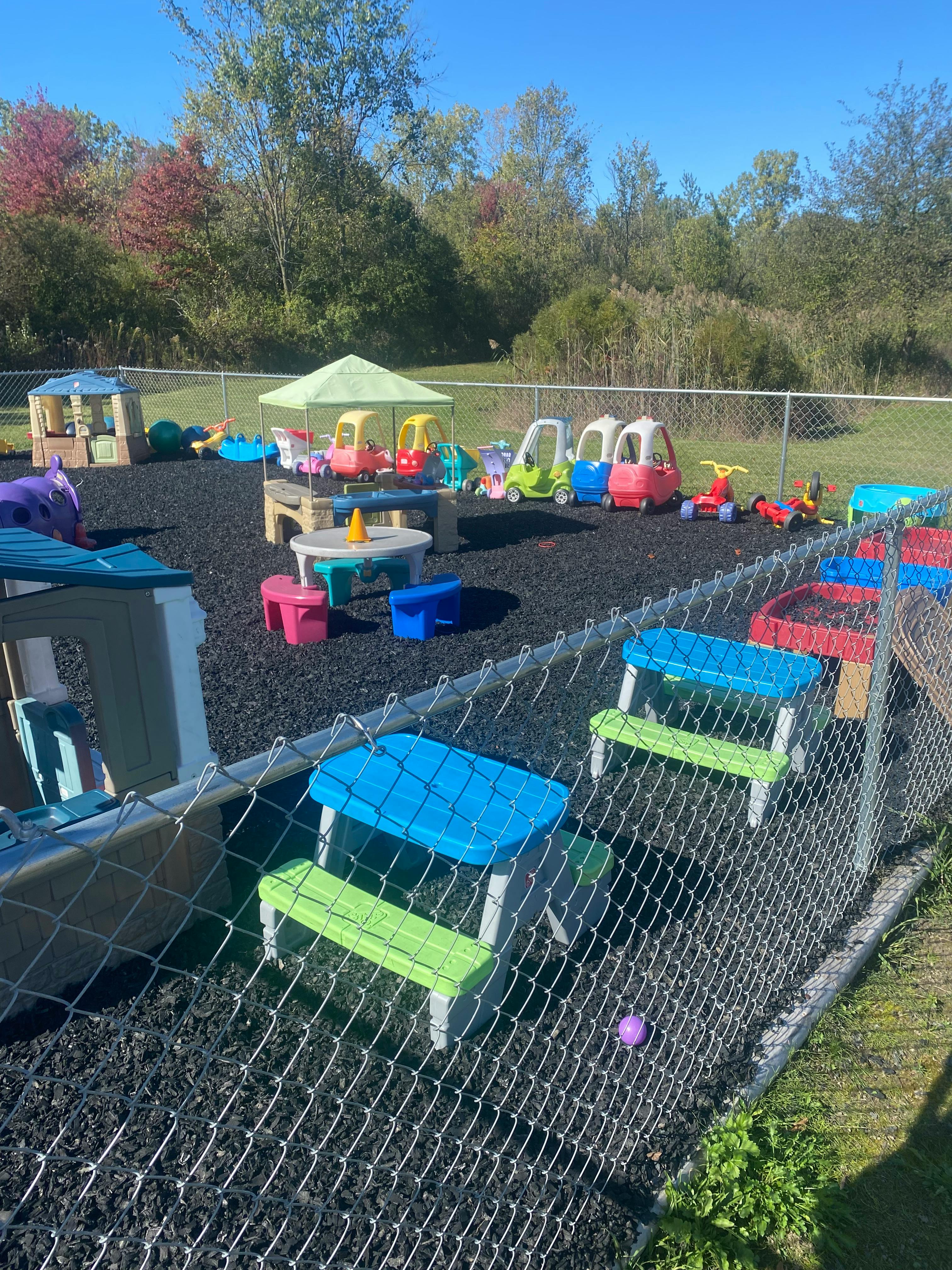 Colorful playground equipment and toys on black wood chips, fenced area