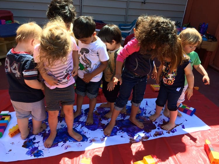 Group of children standing barefoot in purple paint on a white sheet