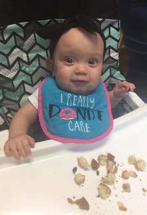 Child in a high chair wearing a bib that says "I REALLY DONUT CARE"