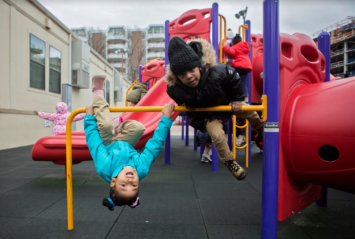 Child hanging upside down on playground bar, another child on bar